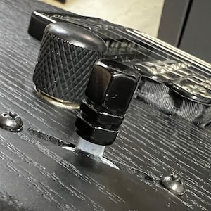 Könnte beinhalten: Nahaufnahme einer schwarzen Gitarre mit zwei Knöpfen. Die Knöpfe sind aus Metall und haben eine strukturierte Oberfläche. Die Gitarre ist aus Holz und hat eine schwarze Oberfläche.