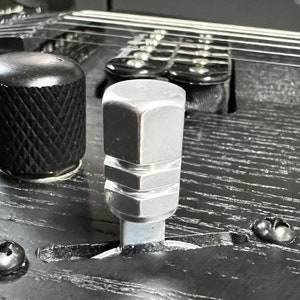 以下が含まれることがあります： 黒い表面に、六角形の頭部を持つ銀色の金属製トグルスイッチが取り付けられています。スイッチはオフの位置です。