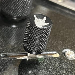 Peut inclure: Bouton noir avec un signe de main "Je t'aime" blanc dessus.