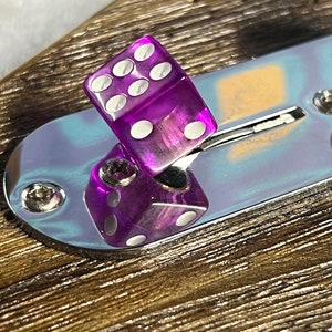 Op de afbeelding: Een paarse dobbelsteen met witte stippen zit op een zilveren schakelaar. De schakelaar is gemonteerd op een bruin houten oppervlak.