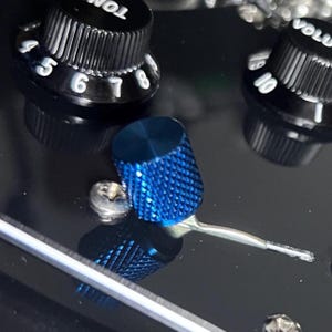 May include: Close-up of a black guitar with blue knobs and silver hardware. The blue knobs have a textured surface. The guitar's volume and tone controls are visible.