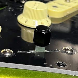 Puede incluir: Primer plano de una perilla negra con una palanca plateada sobre una superficie negra. La perilla está rodeada por un borde plateado y una perilla blanca con los números del 1 al 4.