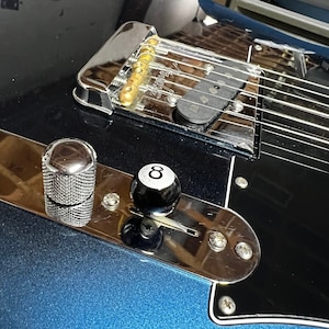 Puede incluir: Primer plano de una guitarra eléctrica negra con un puente cromado y una perilla negra en forma de bola de billar número 8.