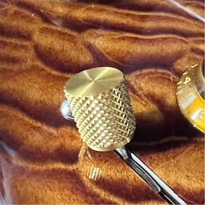 May include: A gold-colored, knurled knob with a diamond pattern. The knob is attached to a silver shaft.