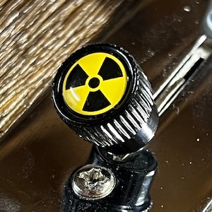 May include: A black knob with a yellow and black radiation symbol. The knob is attached to a metal surface.