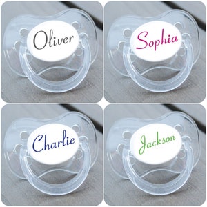 May include: Four clear plastic dummies with white round inserts. Each insert has a different name written in a colourful font: Oliver, Sophia, Charlie, and Jackson.