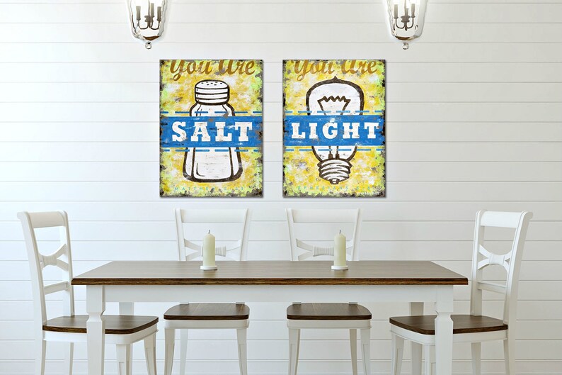 May include: Two framed prints with a yellow background and blue accents. The left print features a salt shaker with the text "You are Salt". The right print features a light bulb with the text "You are Light".