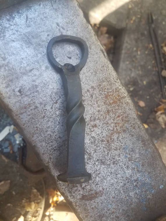 A retired railroad spike forged into a church-key bottle opener — industrial history you can hold in your hand and crack a cold one with.