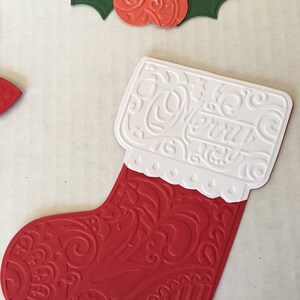 May include: A red and white Christmas stocking with an intricate embossed design. The stocking is decorated with a white cuff and a scalloped edge.