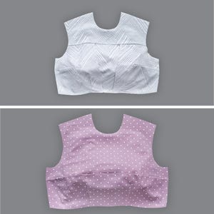 Könnte beinhalten: Zwei ärmellose Oberteile. Das obere ist weiß mit einem strukturierten Zickzackmuster. Das untere Oberteil ist lavendelfarben mit einem weißen Tupfenmuster. Beide Oberteile haben einen Rundhalsausschnitt und werden auf grauem Hintergrund gezeigt.