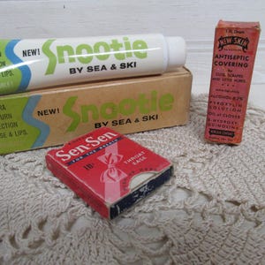 May include: A vintage Snootie by Sea & Ski tube and box with green and blue text, a red Sen-Sen throat ease box, and a tall orange New-Skin antiseptic covering box. The items feature various printed text including product names and usage details.