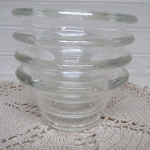 May include: A clear, vintage glass bowl with a unique, stacked design. The bowl features a series of rounded, horizontal ridges, creating a layered effect. The glass is transparent, allowing light to pass through. The bowl is likely used for serving or display.