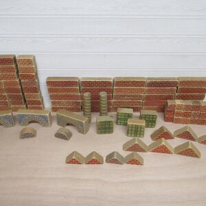 May include: A collection of wooden building blocks featuring printed red brick patterns, green grid patterns, and blue stone textures. The set includes rectangular bricks, arched pieces, cylindrical columns, triangular roof sections, and small semi-circles.