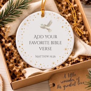 May include: A round white ceramic ornament featuring a gold star pattern border and a central illustration of a white dove carrying an olive branch. The text reads ADD YOUR FAVORITE BIBLE VERSE and MATTHEW 19:26 in black serif font.
