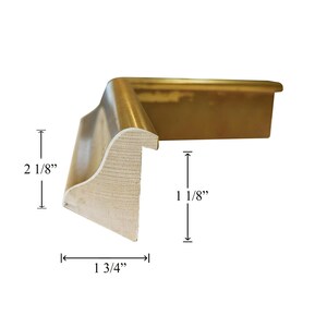 May include: A gold-toned L-shaped picture frame corner sample with a curved profile. The frame features a height of 2 1/8 inches, a width of 1 3/4 inches, and an inner depth of 1 1/8 inches as indicated by the visible measurement markings.