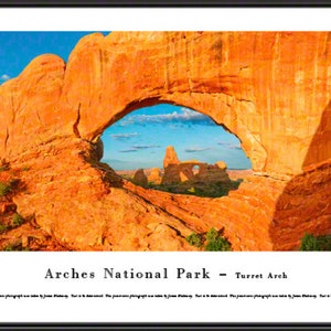 May include: A panoramic view of a large natural sandstone arch in Arches National Park, Utah. The arch is a bright orange color and the sky is a bright blue. The arch is called "Turret Arch".