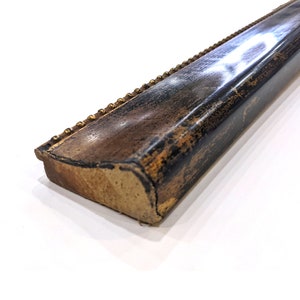 May include: A close-up of a black and gold picture frame molding with a decorative beaded edge.