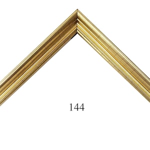 May include: A gold-colored picture frame corner sample featuring a multi-tiered, stepped profile with a metallic finish. The frame section is angled to form a V-shape and includes the number 144 printed in black text below the inner corner.