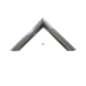 May include: A silver-toned metal picture frame corner sample featuring a clean, angled profile with a smooth, reflective finish. The piece is marked with the number 24 in a simple black font, indicating a specific style or model for framing.