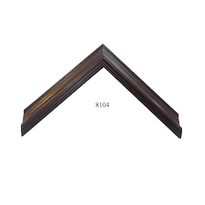 May include: A dark brown picture frame corner sample with a stepped, tiered profile and a smooth finish. The frame features a distinct angular shape and is labeled with the number 8104 printed in black text in the center of the open space.