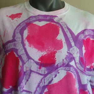 May include: White long-sleeved shirt with a tie-dye pattern in shades of pink and purple. The design features abstract shapes and swirls.