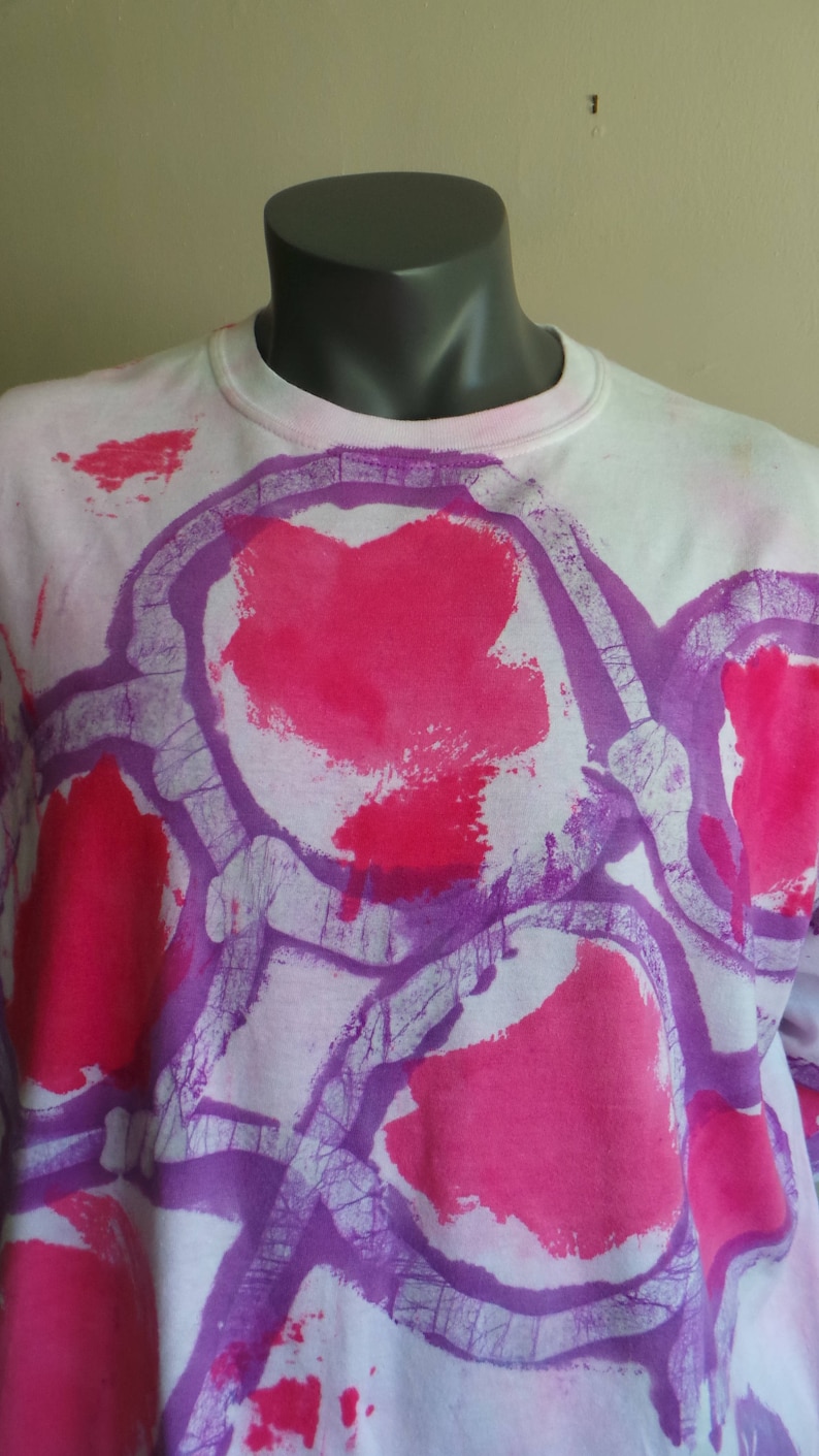 May include: White long-sleeved shirt with a tie-dye pattern in shades of pink and purple. The design features abstract shapes and swirls.