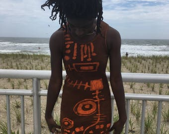 Puede incluir: Una persona lleva un vestido marrón sin mangas con patrones geométricos naranjas. El vestido tiene una silueta ajustada y un escote redondo.
