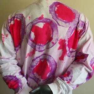 May include: White long-sleeved shirt with a pink and purple abstract print. The print features large circles with a pink centre and a purple outline.