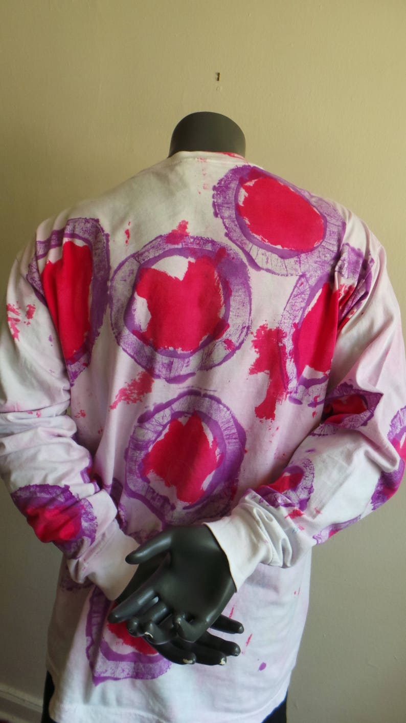 May include: White long-sleeved shirt with a pink and purple abstract print. The print features large circles with a pink centre and a purple outline.