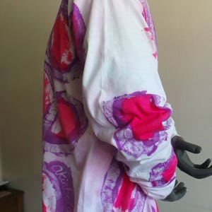 May include: White long-sleeved shirt with a tie-dye pattern in shades of pink and purple. The shirt has a circular design with the word "Okidata" written on the side.
