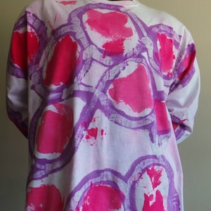 May include: White long-sleeved shirt with a tie-dye pattern of pink and purple circles.