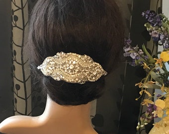 May include: A silver hair comb with a large, ornate design featuring clear rhinestones. The comb is on a mannequin's head, with the back of the head facing the camera.