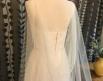 May include: A white tulle wedding veil with a single layer of tulle and a scalloped edge. The veil is draped over a white dress form.