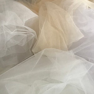 May include: A pile of white and beige tulle fabric. The fabric is soft and delicate, and it is perfect for crafting or sewing.