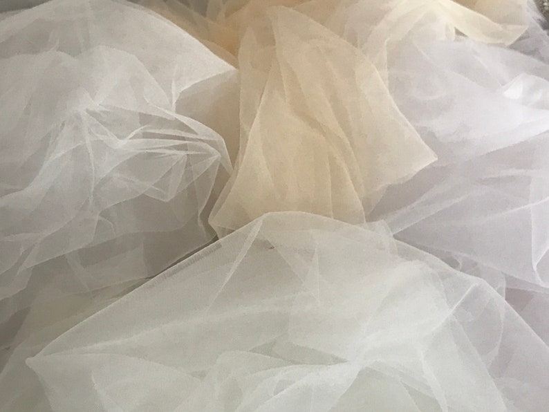 May include: A pile of white and beige tulle fabric. The fabric is soft and delicate, and it is perfect for crafting or sewing.
