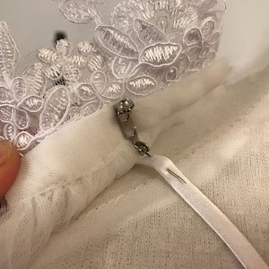 May include: White lace trim with a white fabric loop and a silver safety pin.