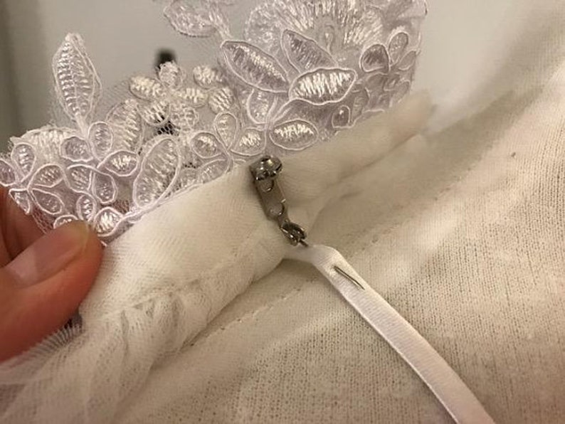 May include: White lace trim with a white fabric loop and a silver safety pin.