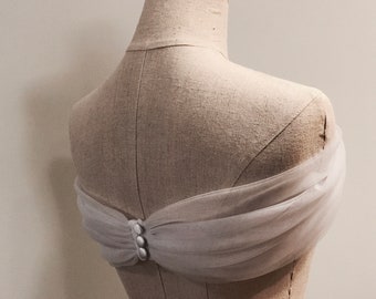 May include: White tulle fabric draped over a dress form, secured with buttons in the back.