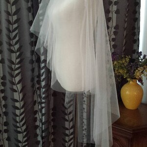 May include: A white tulle wedding veil with a single layer and a scalloped edge. The veil is draped over a white dress form.