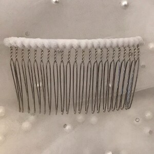 May include: A silver hair comb with a white padded base. The comb has 18 teeth.