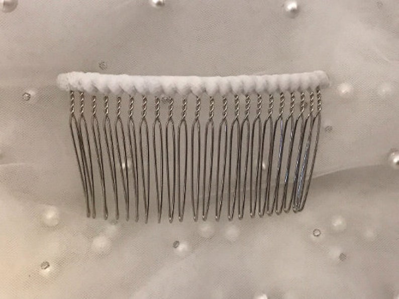 May include: A silver hair comb with a white padded base. The comb has 18 teeth.