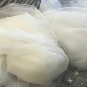 May include: Two pieces of white tulle fabric, folded and arranged on a gray and white patterned surface.