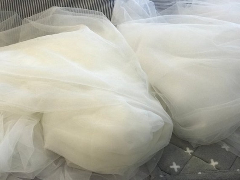 May include: Two pieces of white tulle fabric, folded and arranged on a gray and white patterned surface.
