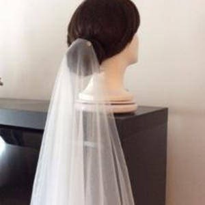 May include: A white bridal veil made of tulle, with a single pearl embellishment at the top. The veil is draped over a mannequin head, with the veil flowing down the back.