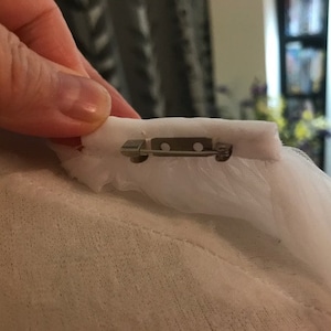 May include: A white tulle fabric with a silver safety pin attached to it.