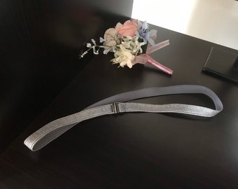 May include: A silver glitter headband with a grey elastic band. The headband is lying on a black surface.