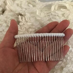 May include: A hair comb featuring a row of thin, silver-toned metal teeth attached to a white, textured, cylindrical top bar. The comb is designed for securing hair and has a simple, functional structure with fourteen individual metal prongs.