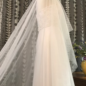 Op de afbeelding: Een witte bruids sluier van tule met een delicate kantversiering. De sluier is gedrapeerd over een witte paspop.