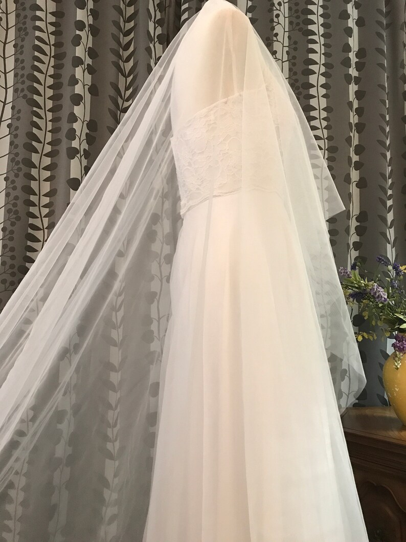 Op de afbeelding: Een witte bruids sluier van tule met een delicate kantversiering. De sluier is gedrapeerd over een witte paspop.