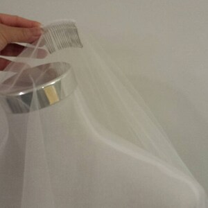 May include: A white tulle veil with a comb attached to the top edge. The veil is draped over a mannequin head.